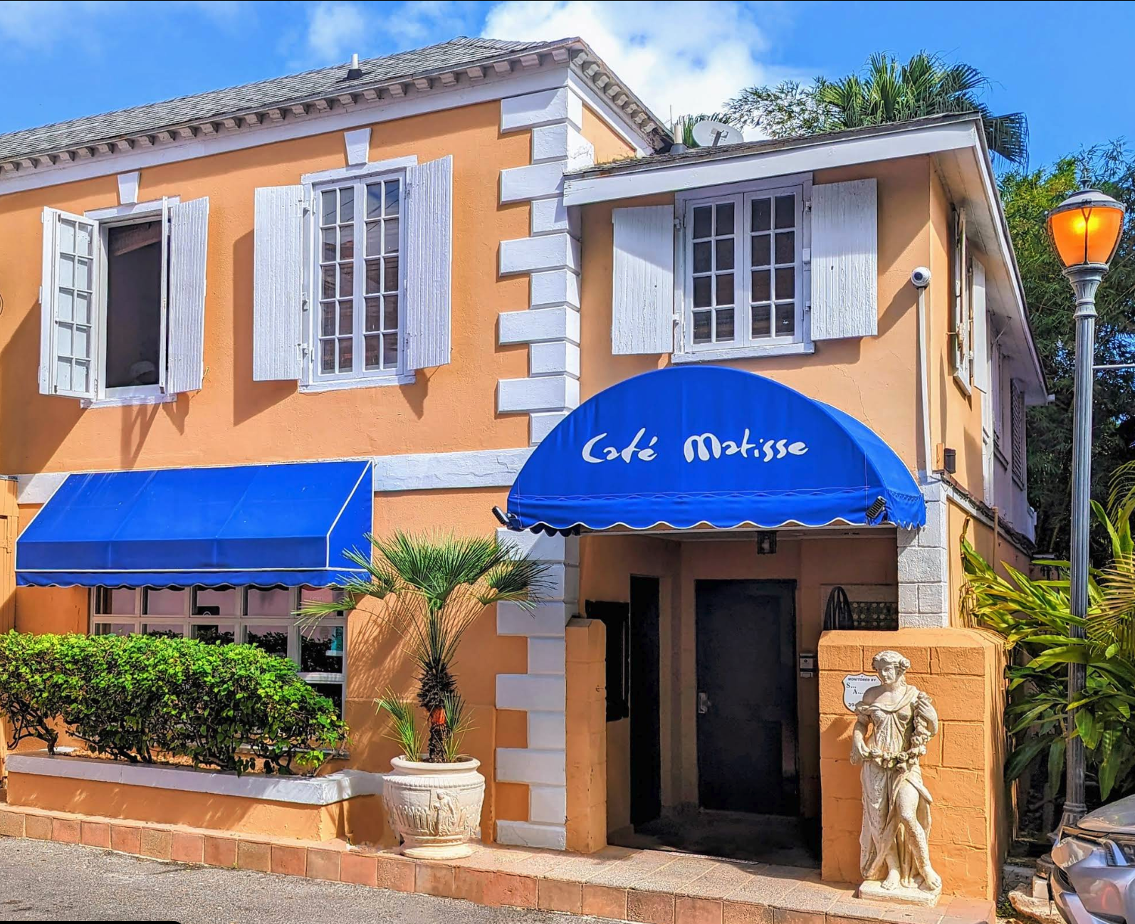 Café Matisse exterior with white shutters and a blue entrance awning in Nassau