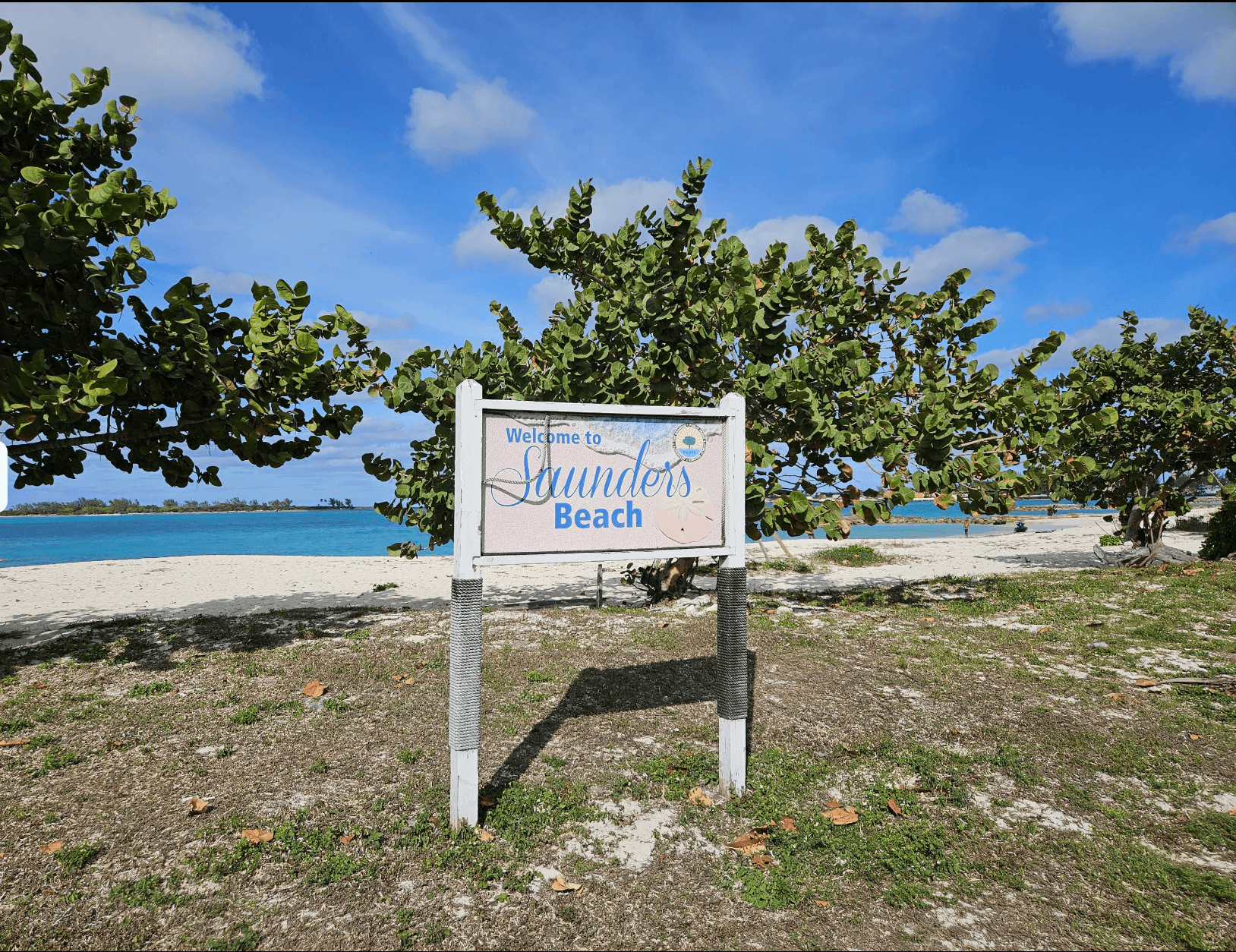 Saunders Beach welcome sign with sand and turquoise water behind it